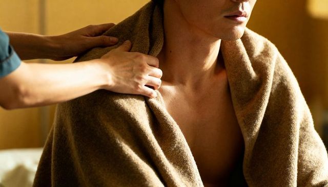 Wrapping asian man in warm brown towel, caring hands adjusting fabric for comfort