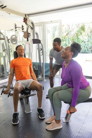 African american small group training with personal trainer in bright home gym using dumbbells