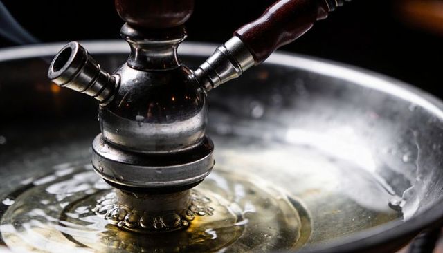 Close-up hookah stem bubbling in reflective tray, concentric ripples and metal shine