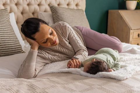 Mother bonding with newborn on cozy bed holding hand, nurturing maternal moment