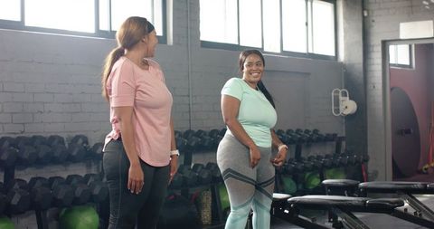 Women training together in sunlit gym sharing conversation and workout motivation