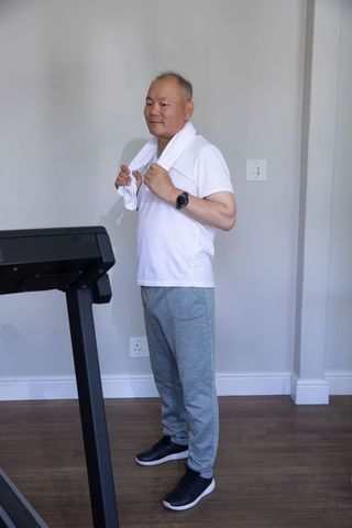 Senior chinese man cooling down after treadmill workout checking smartwatch in home gym