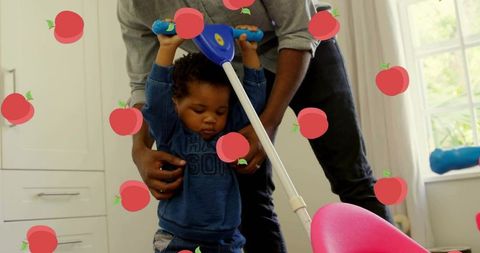 Father assisting baby with walker indoors amidst graphic apples