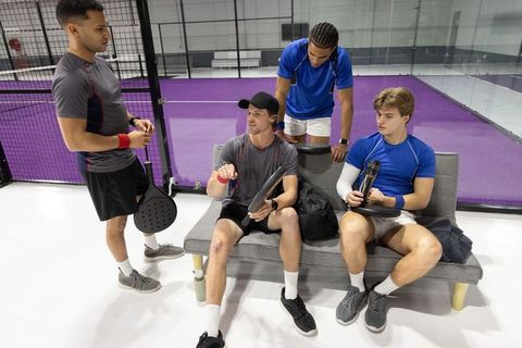 Padel teammates resting and strategizing on bench at purple indoor court with paddles