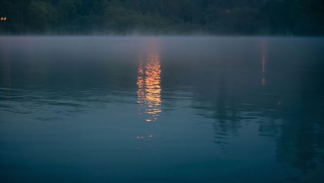 Golden lantern reflection shimmering on misty twilight lake with forest silhouette