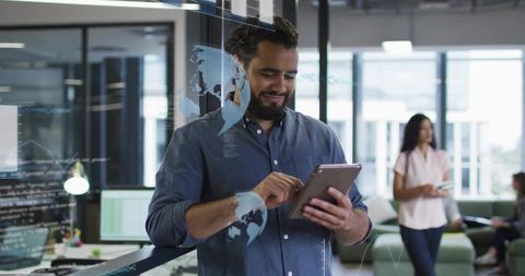 Smiling bearded professional using tablet in modern open-plan office with digital overlays