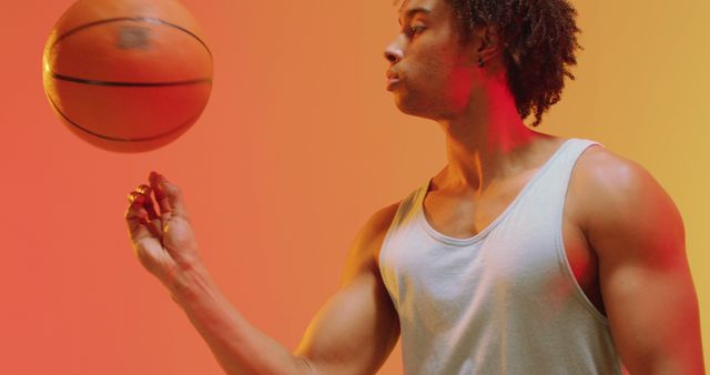This image features an athletic young man wearing casual sportswear, spinning a basketball on his finger against a vibrant gradient background. Ideal for use in sports advertisements, fitness and health blogs, motivational posters, and athletic lifestyle content.