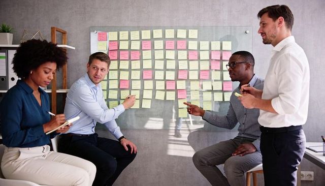 Multiracial team brainstorming at glass board with colorful sticky notes in modern office