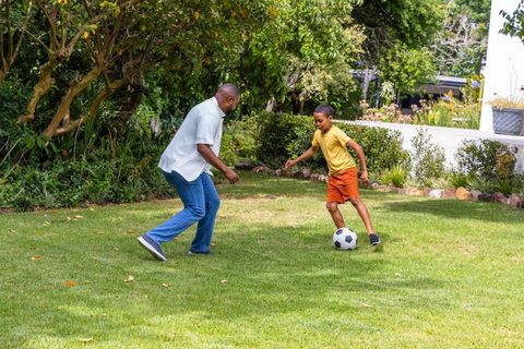 African american father playing soccer with son on backyard lawn casual summer family moment