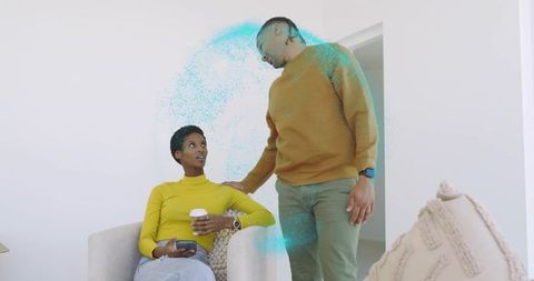 Couple relaxing in minimalist living room holding coffee and smartphone, man leaning in