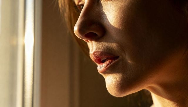 Woman gazing out window, face lit by warm sunlight, closeup profile and jawline