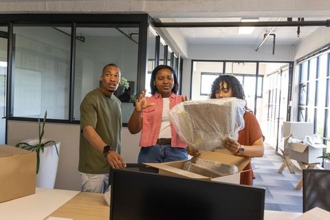 African american coworkers unpacking monitor and setting up open-plan office workstation