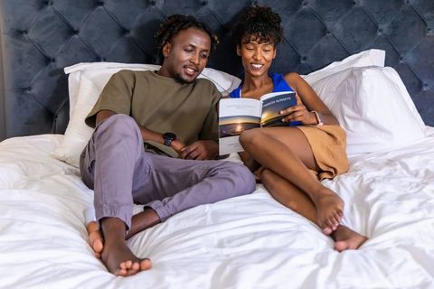 African american couple relaxing in bed reading sunset book together on tufted headboard