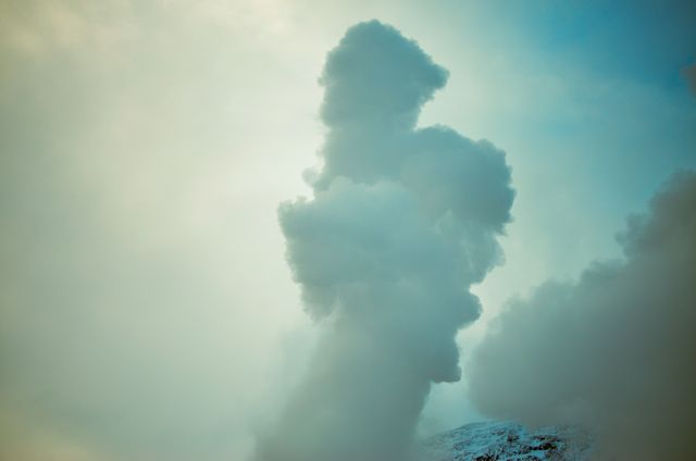 Majestic billowing smoke rises above a snow-covered mountain, creating a dramatic and mysterious atmosphere. This image can be used to illustrate concepts related to nature, environment, mountainous regions, pollution, and clean air initiatives. The serene and atmospheric sky complements environmental campaigns, adventure travel content, weather forecasts, and storytelling imagery.