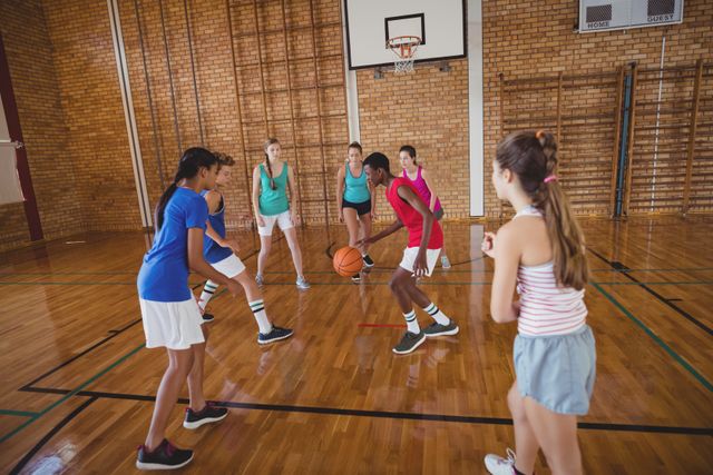 Group of high school students in athletic wear actively playing basketball on an indoor court. Perfect for use in content related to education, youth sports, teamwork, fitness, physical education programs, and school environments. Vibrant and energetic, showcasing determination and engagement in sports.