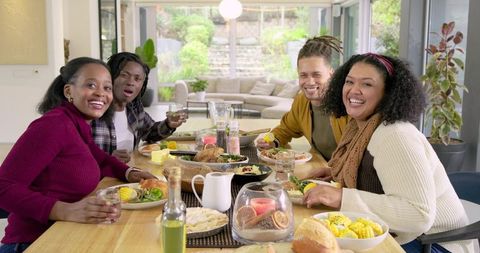 Diverse friends gathering around wooden dining table sharing joyful homemade dinner