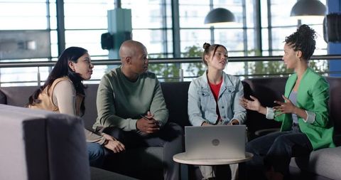 Diverse team discussing project around laptop in modern office lounge brainstorming