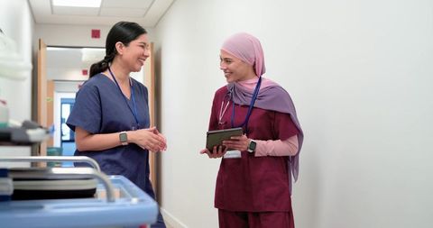 Diverse female nurses collaborating while reviewing tablet in hospital corridor, teamwork