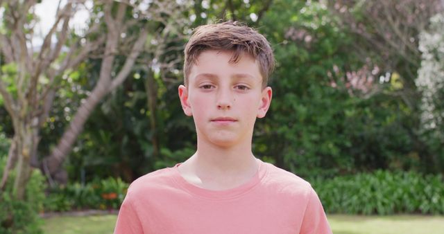 Pre-teen boy standing confidently in a garden filled with trees and greenery on a bright summer day. Could be used in educational content, lifestyle articles, outdoor activity promotions, or family-oriented advertisements.