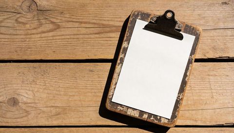 Worn wooden clipboard holding blank white paper on rustic plank table for mockups
