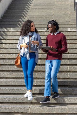 Diverse young adults walking down stone steps talking and using tablet and smartphone