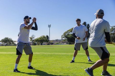Three men practicing baseball batting drill on sunny park field