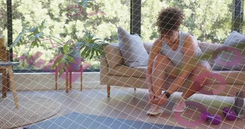 Woman tying sneakers for home workout near window with dumbbells and yoga mat