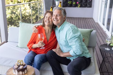 Celebrating 50th anniversary on balcony with mature couple hugging and wine