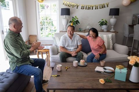 Chinese family celebrating senior woman birthday at home living room party with cupcake and gifts