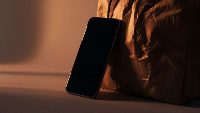 Moody minimal smartphone leaning against crumpled brown paper bag casting soft chiaroscuro glow