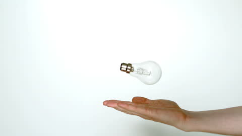 Hand Tossing Lightbulb in Slow Motion Against Plain Background