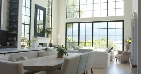 Sunlit minimalist open-plan living featuring solid timber dining table and black grid windows