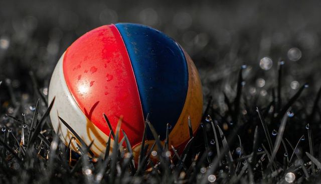 Sitting glossy multicolor rubber ball on dewy grass with morning bokeh and water droplets