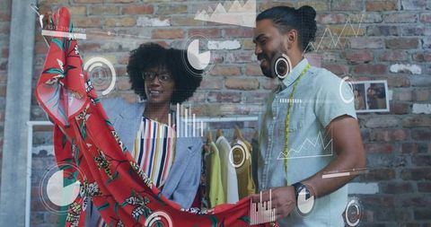 Fashion designers holding vibrant red floral fabric while analyzing digital HUD in studio