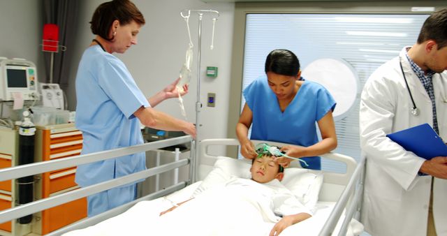 This image depicts a team of healthcare professionals including a doctor and nurses taking care of a child patient in a hospital bed. The doctor appears to review notes while nurses assist with medical treatments and care for the child. This photo can be used for medical and healthcare websites, brochures, hospital advertisements, and educational materials regarding pediatric care.