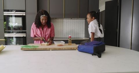 Mother preparing school lunch while child in uniform watching at kitchen island