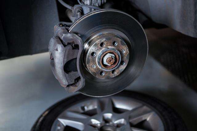 Close-up of car brake disc and caliper in a repair garage. Ideal for use in automotive repair, maintenance services, mechanic workshops, and vehicle engineering content.