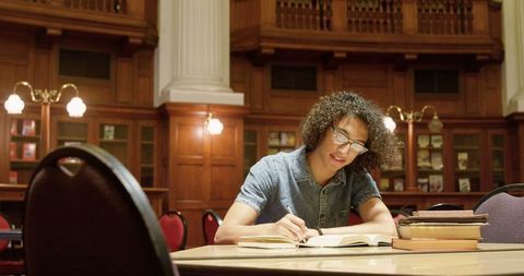 Young man studying in wooden library interior with books