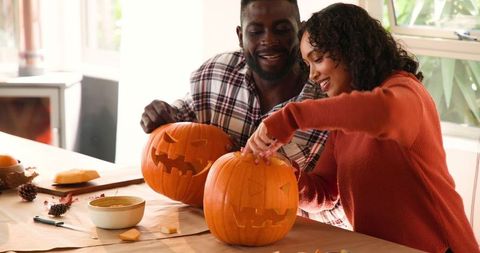 Multiracial Couple Happily Carving Pumpkin Jack-o'-Lanterns for Halloween
