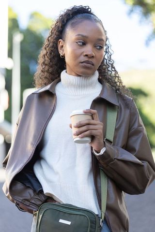 African american woman holding coffee walking in leather jacket and turtleneck