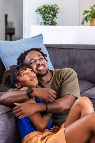 African american couple cuddling on gray sofa in modern living room