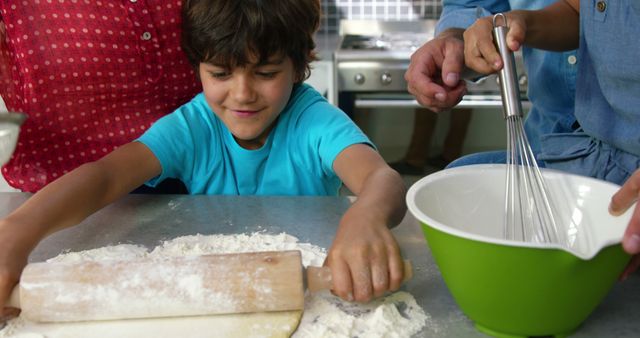 Young boy actively rolling dough on kitchen counter while parent nearby holding whisk in bowl. Perfect for promoting family bonding, showcasing home cooking activities, and illustrating hands-on baking projects.