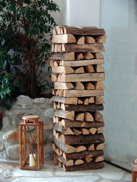 Neatly arranged firewood stack next to a wooden lantern with a candle, set in a rustic indoor interior. Ideal for illustrating concepts of cozy home decor, natural interior designs or autumn and winter preparations. Perfect for use in blogs, magazines, or social media related to home improvement, DIY projects, or eco-friendly living.