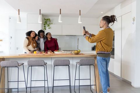 Friends posing at modern kitchen island while friend capturing moment with smartphone
