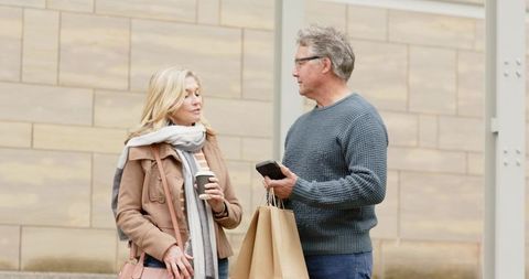 Senior couple chatting while shopping holding coffee bags smartphone urban lifestyle