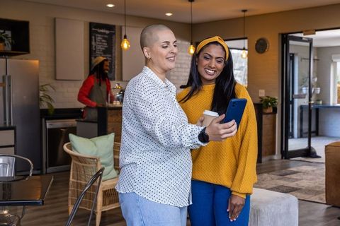 Diverse friends checking phone and laughing in modern coworking lounge with warm tones