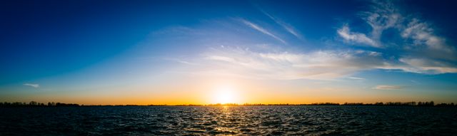 Stunning panoramic view of a sunset over a calm ocean with a golden horizon glowing in the distance. Ideal for usage in travel brochures, websites, or relaxation and meditation materials. Scenic landscape perfect for adding a peaceful and beautiful touch to your project.