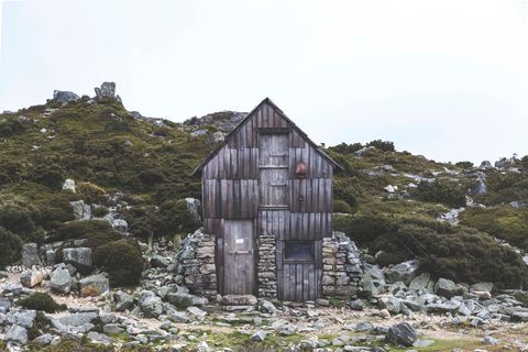 Weathered wooden cabin standing alone among rocky alpine moorland with mossy boulders