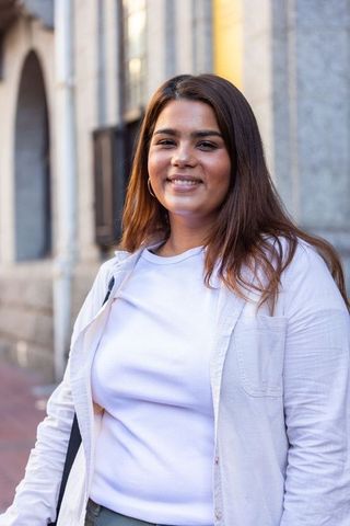 Smiling young woman in white ribbed t-shirt urban sidewalk by stone arches golden hour
