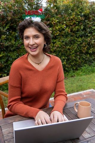 Young woman wearing merry christmas headband typing on laptop in cozy garden workspace
